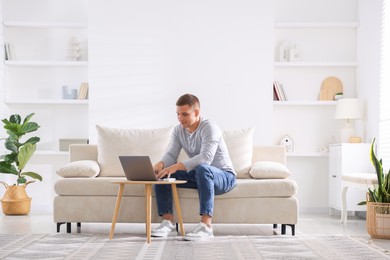 Photo of Young man using laptop on sofa at home