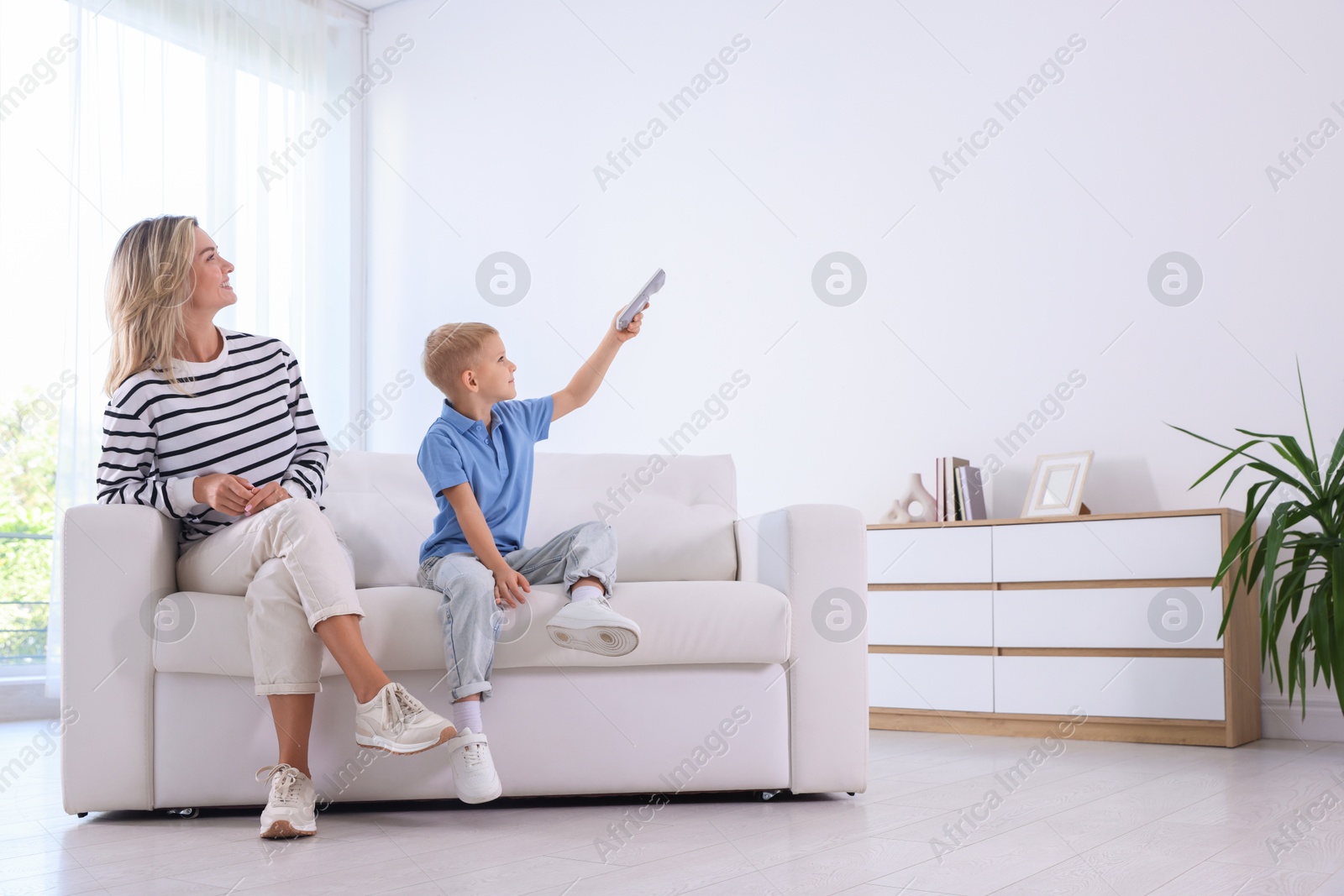 Woman and her son using remote to control air conditioner on sofa at home Photo of Woman and her son using remote to control air conditioner on sofa at home