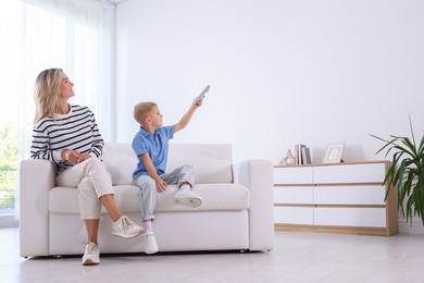 Photo of Woman and her son using remote to control air conditioner on sofa at home