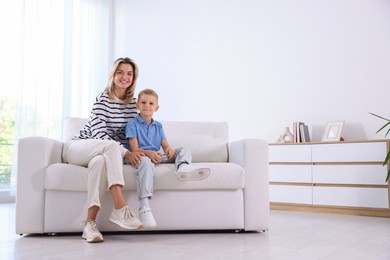 Photo of Woman and her son with air conditioner remote control on sofa at home