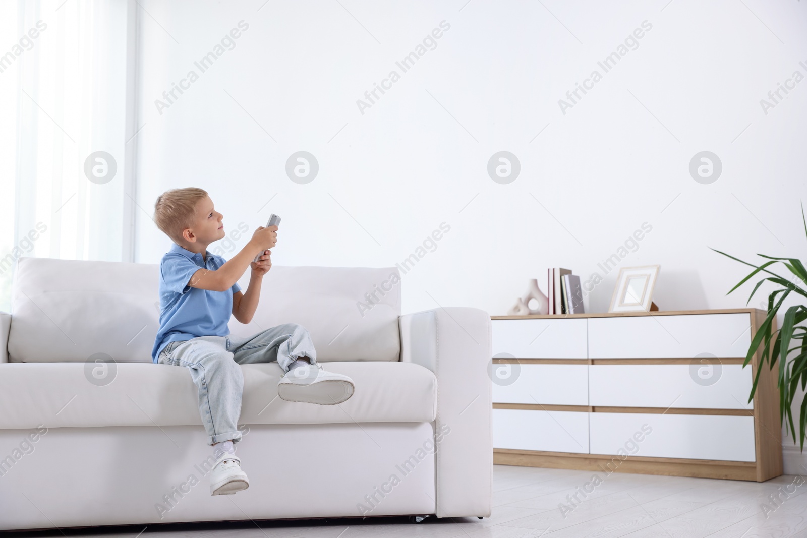 Cute little boy using remote to control air conditioner on sofa at home Photo of Cute little boy using remote to control air conditioner on sofa at home