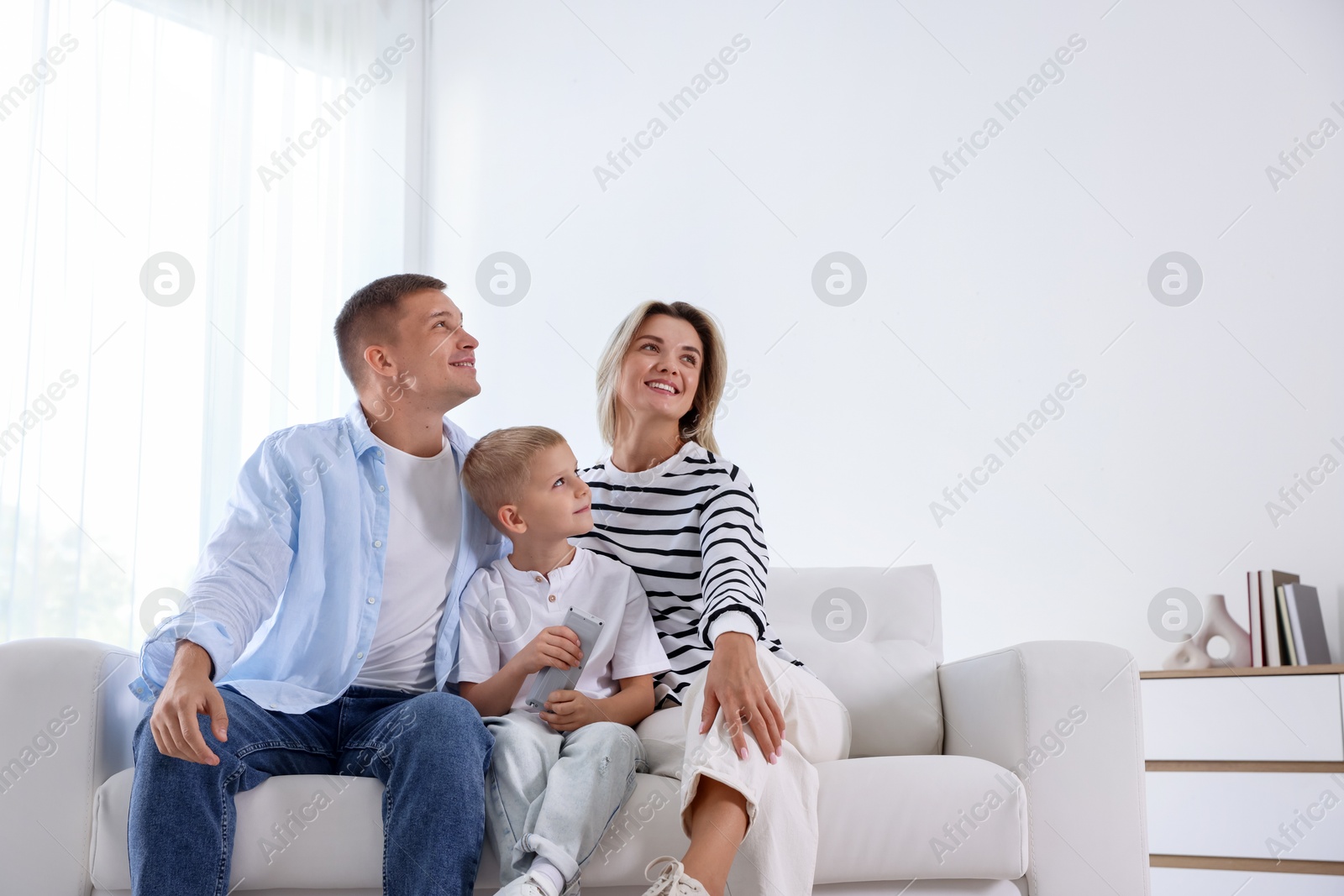 Photo of Little boy with air conditioner remote control and his parents on sofa at home