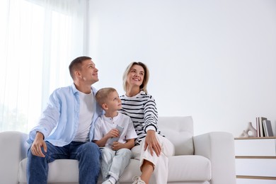 Photo of Little boy with air conditioner remote control and his parents on sofa at home