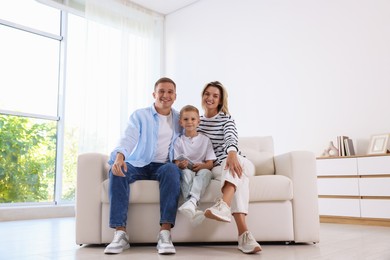 Photo of Little boy with air conditioner remote control and his parents on sofa at home