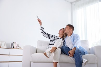 Photo of Man and woman using remote to control air conditioner on sofa at home
