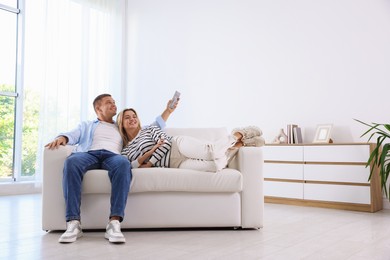 Photo of Woman and man using remote to control air conditioner on sofa at home