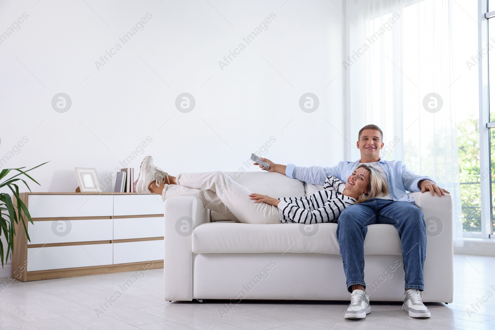 Woman and man with air conditioner remote control on sofa at home Photo of Woman and man with air conditioner remote control on sofa at home