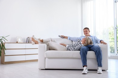 Photo of Woman and man with air conditioner remote control on sofa at home