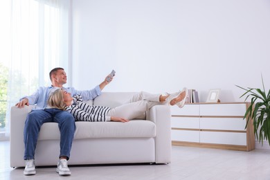 Photo of Woman and man using remote to control air conditioner on sofa at home