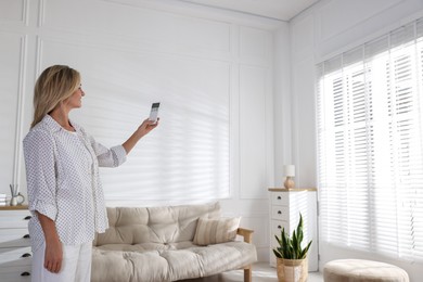 Photo of Woman using remote to control air conditioner at home. Space for text