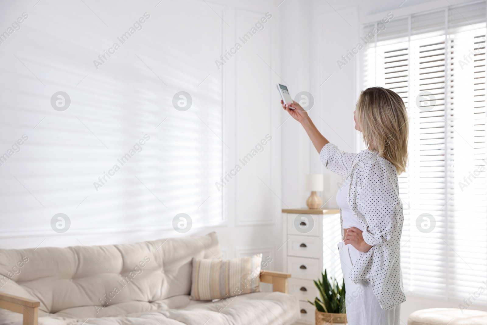 Photo of Woman using remote to control air conditioner at home. Space for text