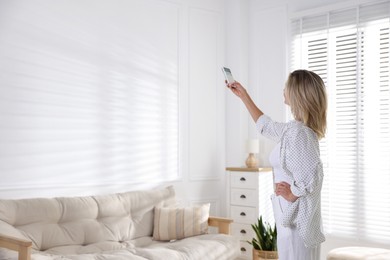 Photo of Woman using remote to control air conditioner at home. Space for text