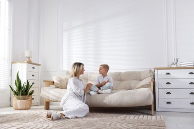Photo of Woman and her son with air conditioner remote control on sofa at home