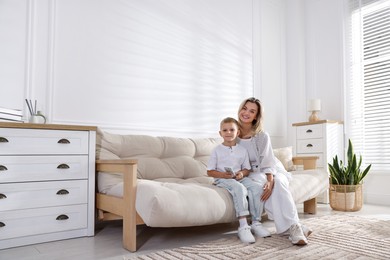 Photo of Woman and her son with air conditioner remote control on sofa at home