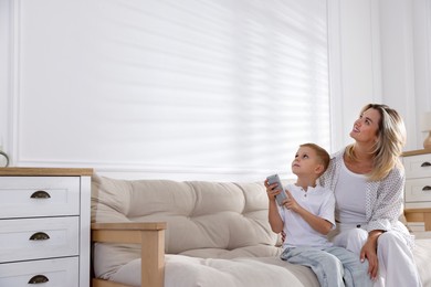 Photo of Woman and her son using remote to control air conditioner on sofa at home