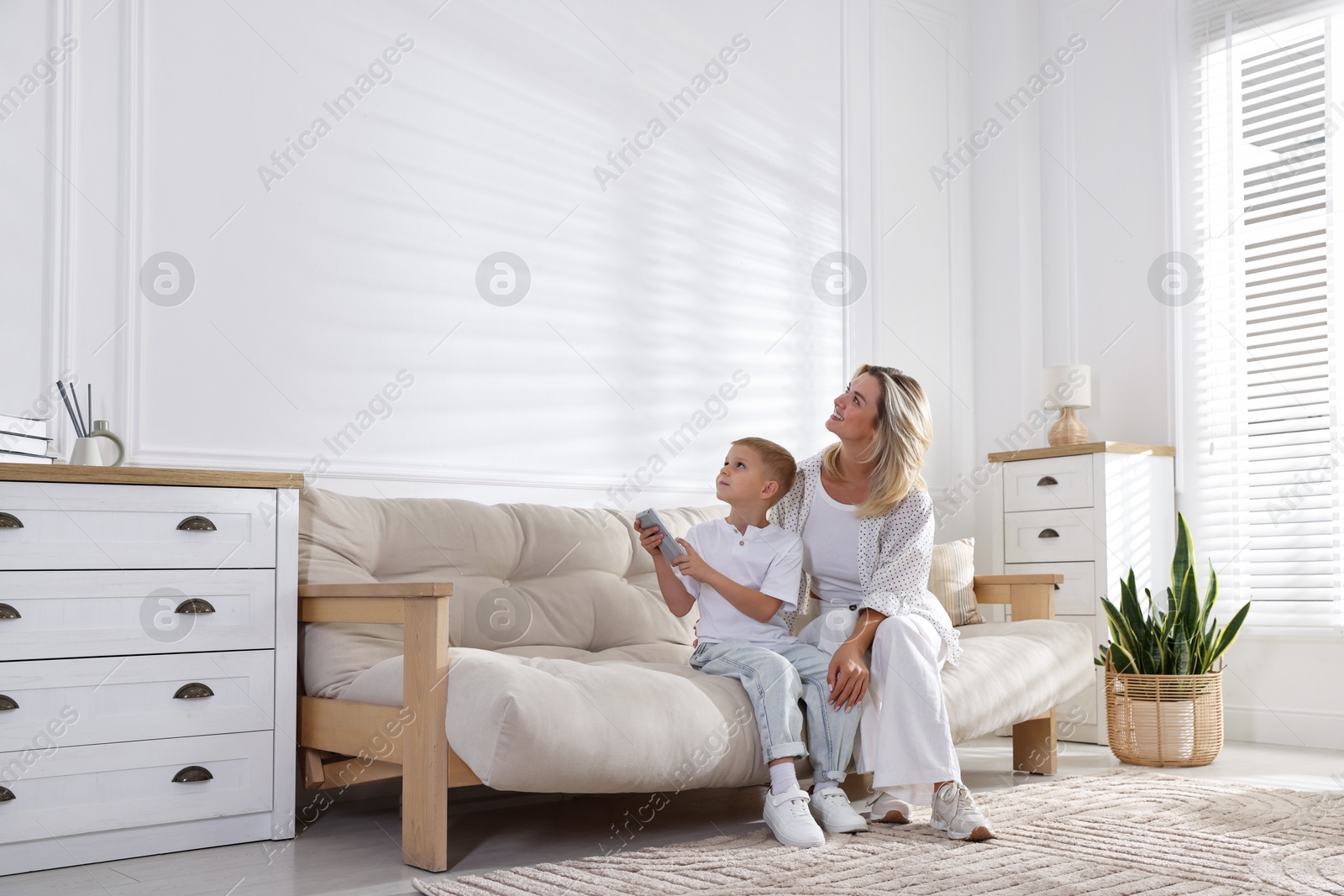 Woman and her son using remote to control air conditioner on sofa at home Photo of Woman and her son using remote to control air conditioner on sofa at home