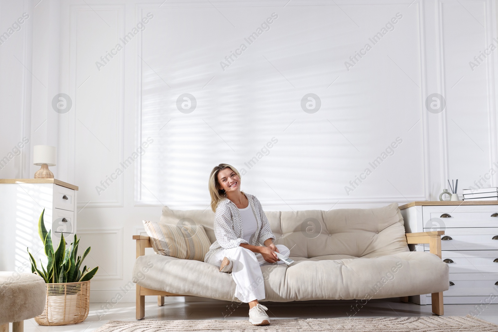 Photo of Woman with air conditioner remote control on sofa at home