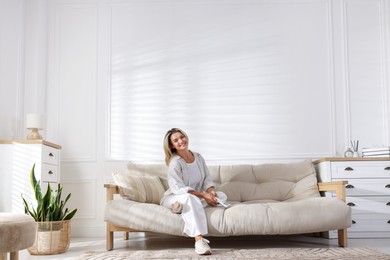 Photo of Woman with air conditioner remote control on sofa at home
