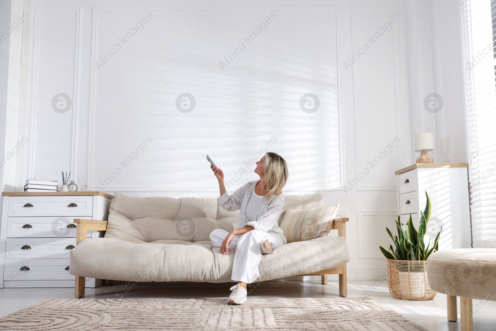 Photo of Woman using remote to control air conditioner at home