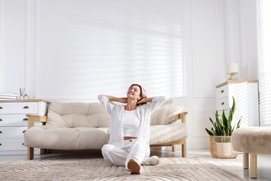 Photo of Beautiful woman sitting on rug near sofa at home