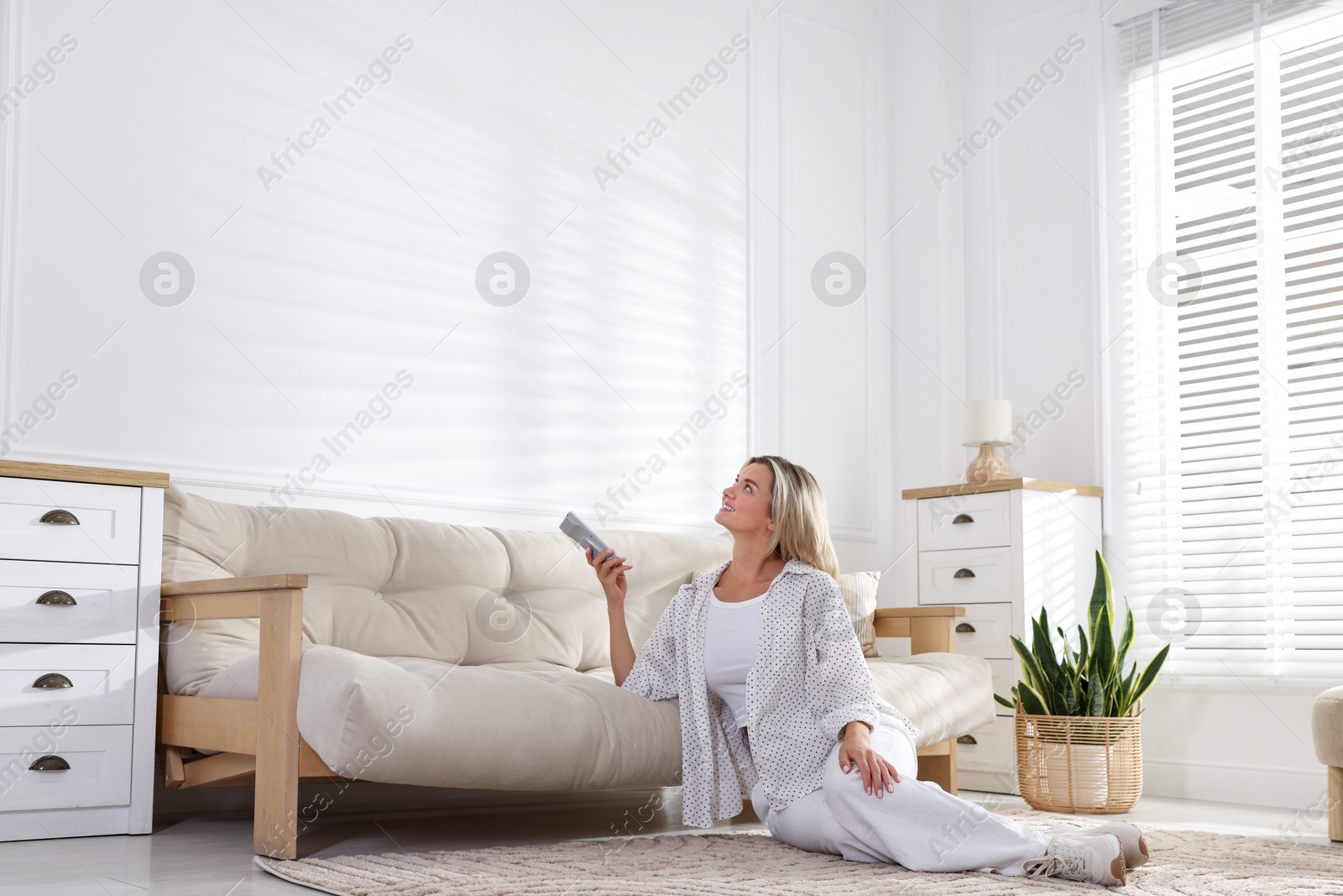 Photo of Woman using remote to control air conditioner at home
