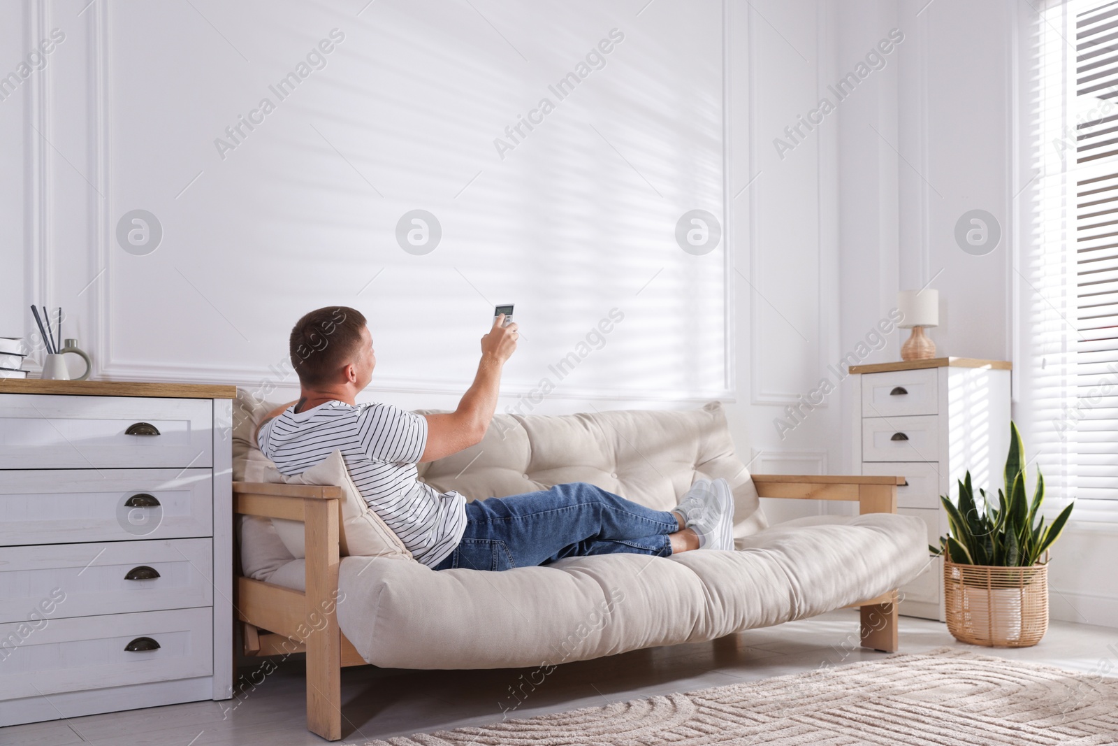 Man using remote to control air conditioner on sofa at home Photo of Man using remote to control air conditioner on sofa at home