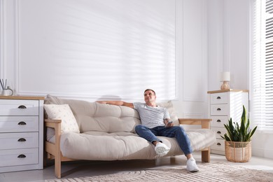 Photo of Man with air conditioner remote control on sofa at home