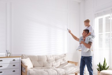 Photo of Little boy and his father using remote to control air conditioner at home. Space for text