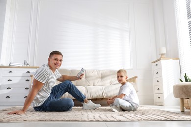 Photo of Cute little boy and his father with air conditioner remote control at home