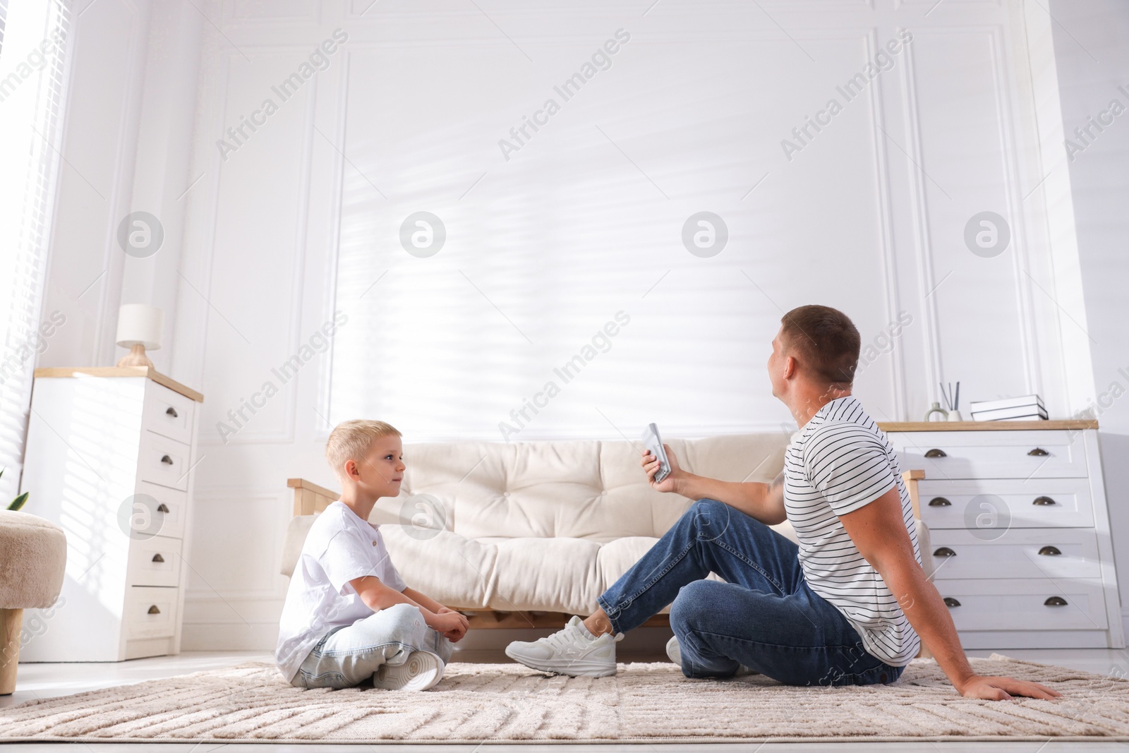 Photo of Cute little boy and his father using remote to control air conditioner at home, low angle view