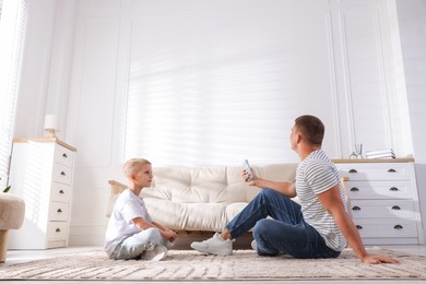 Photo of Cute little boy and his father using remote to control air conditioner at home, low angle view