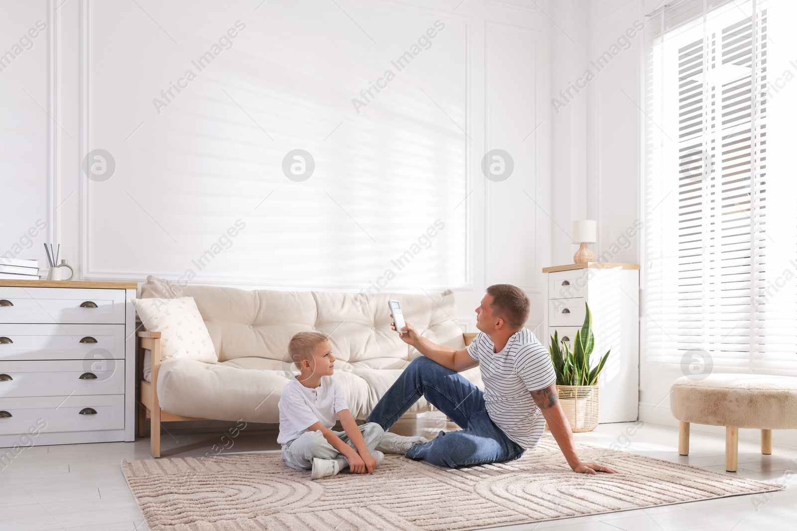 Photo of Cute little boy and his father using remote to control air conditioner at home
