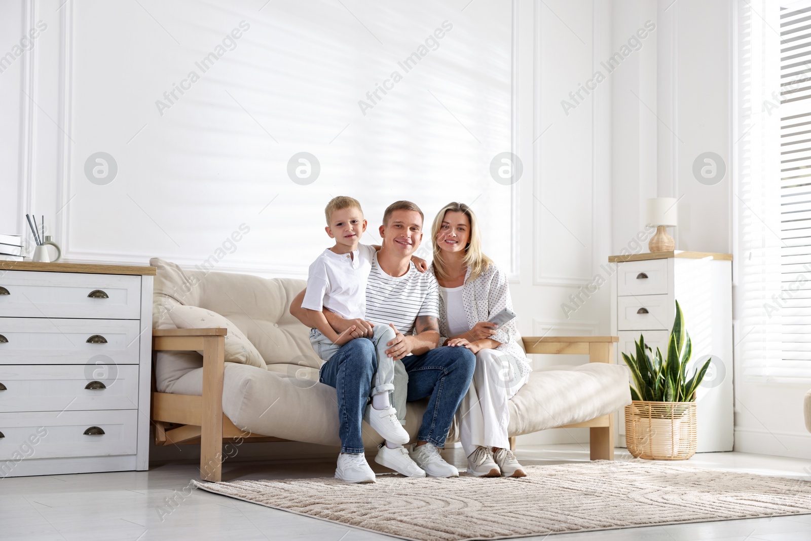 Woman with air conditioner remote control, her husband and son on sofa at home Photo of Woman with air conditioner remote control, her husband and son on sofa at home