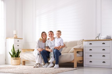 Photo of Woman with air conditioner remote control, her husband and son on sofa at home