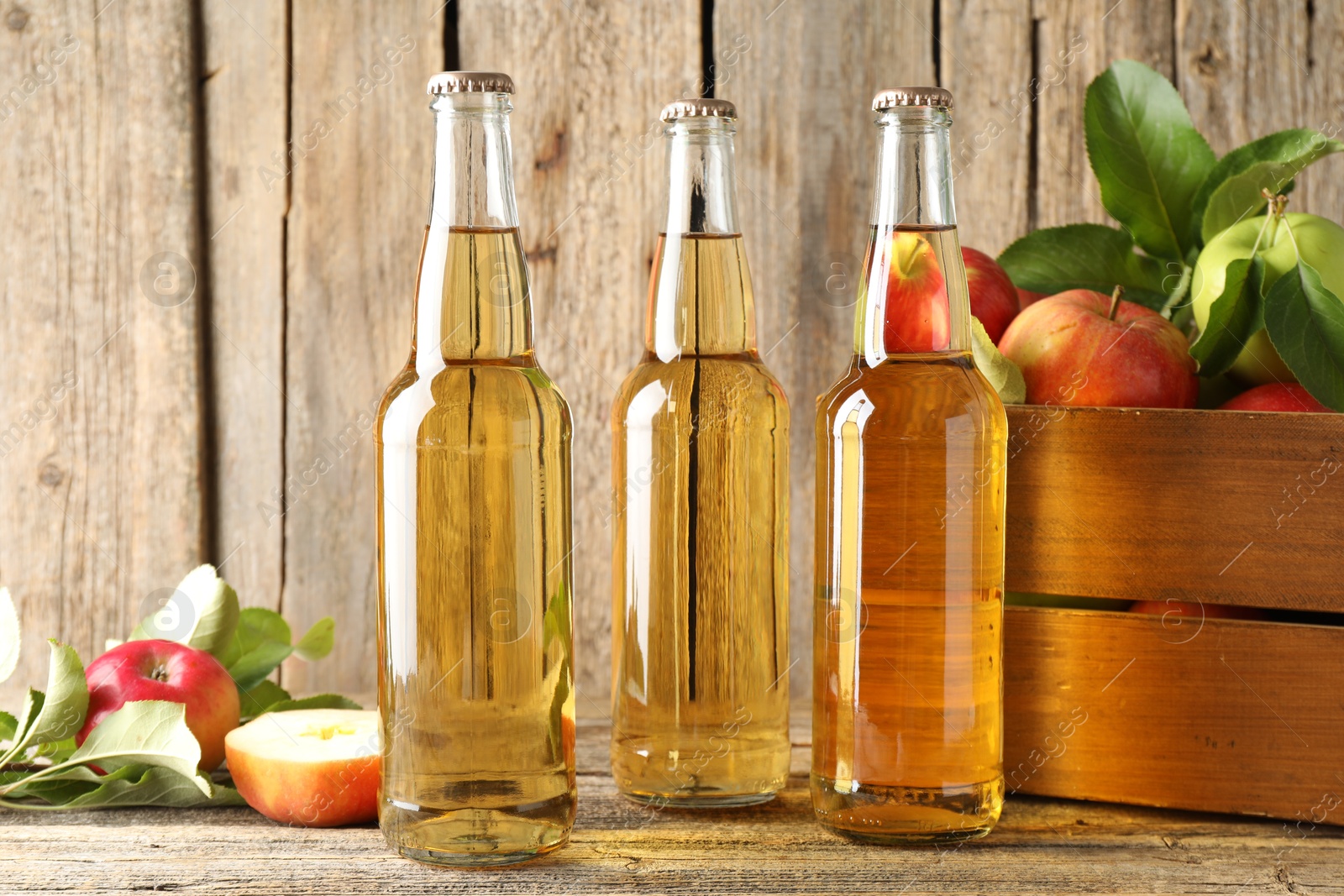 Photo of Delicious cider in glass bottles and apples on wooden table