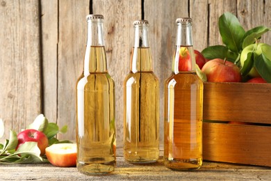 Photo of Delicious cider in glass bottles and apples on wooden table