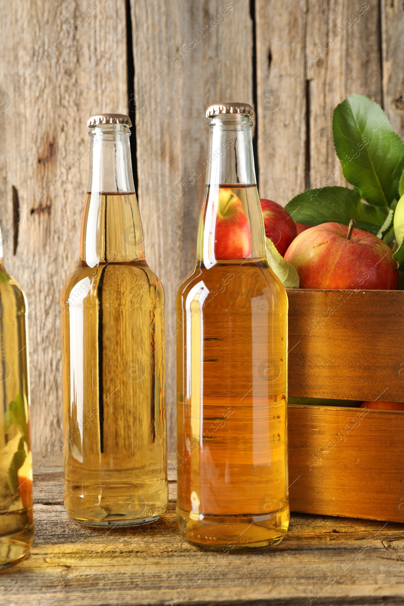 Photo of Delicious cider in glass bottles and apples on wooden table, closeup