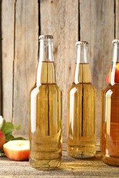 Photo of Delicious cider in glass bottles and apples on wooden table, closeup