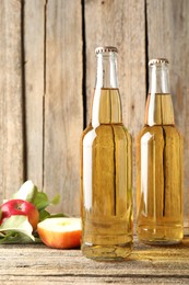 Photo of Delicious cider in glass bottles and apples on wooden table, closeup