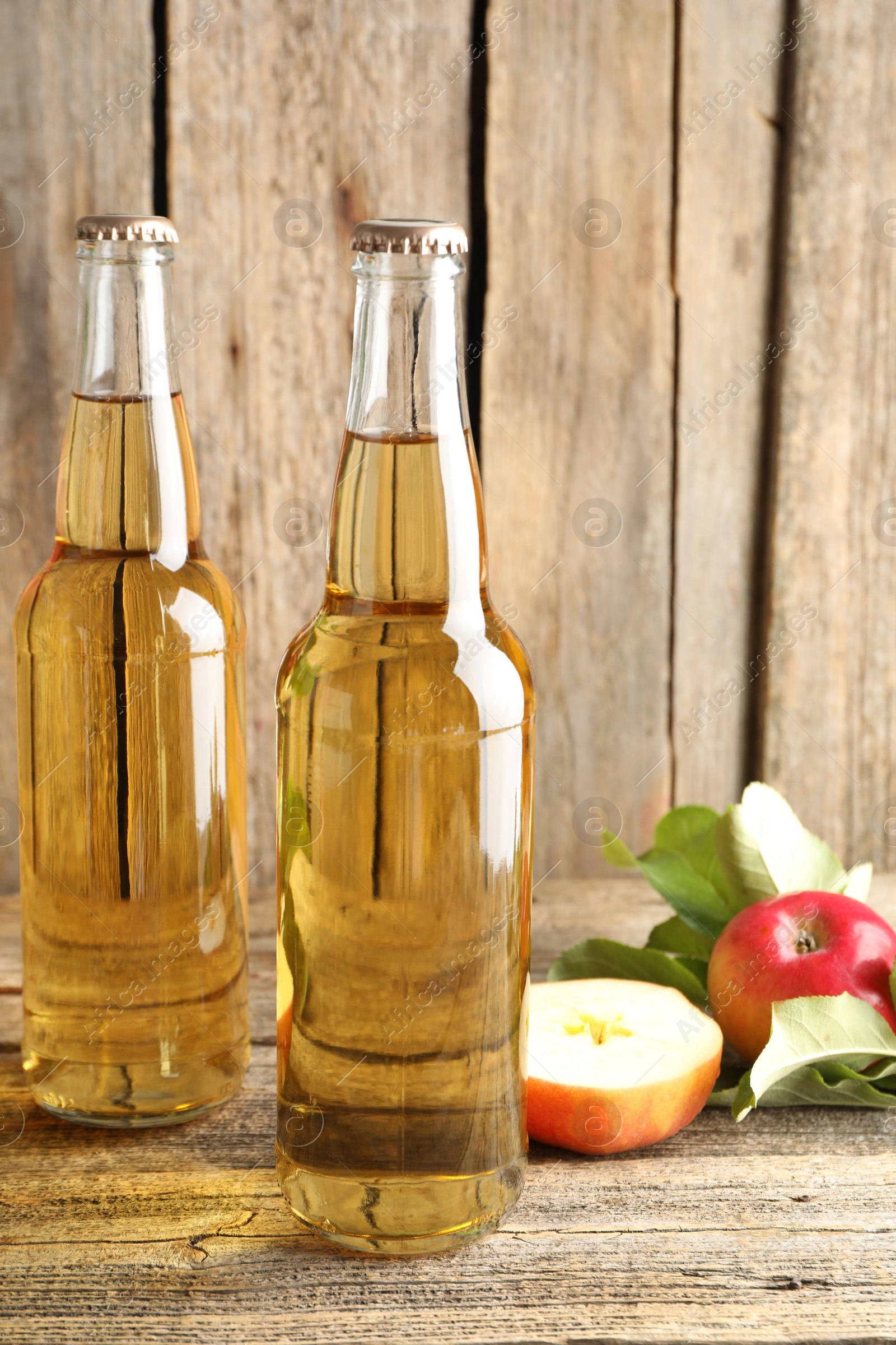 Photo of Delicious cider in glass bottles and apples on wooden table, closeup