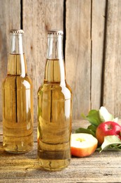 Photo of Delicious cider in glass bottles and apples on wooden table, closeup
