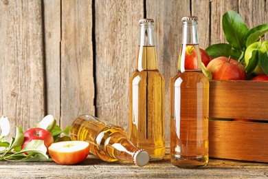 Photo of Delicious cider in glass bottles and apples on wooden table. Space for text