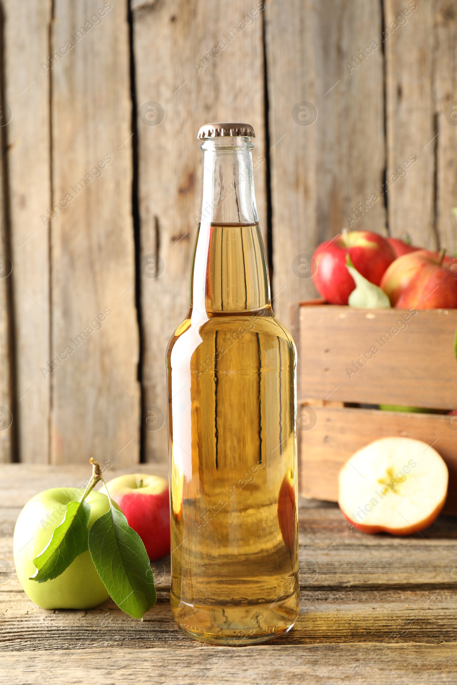 Delicious cider in glass bottle and apples on wooden table Photo of Delicious cider in glass bottle and apples on wooden table