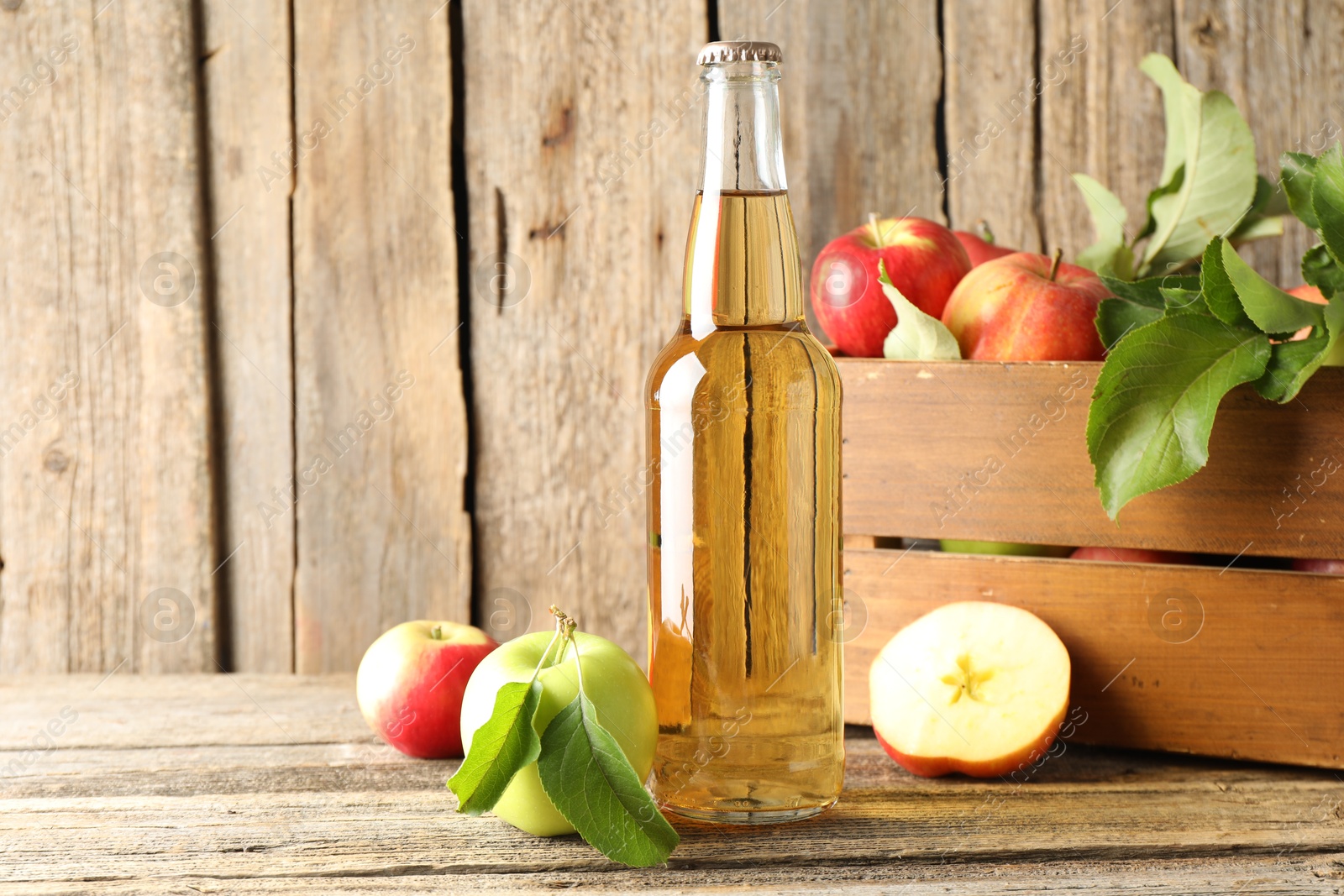 Photo of Delicious cider in glass bottle and apples on wooden table