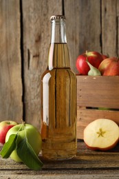 Photo of Delicious cider in glass bottle and apples on wooden table, closeup