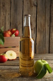 Photo of Delicious cider in glass bottle and apples on wooden table