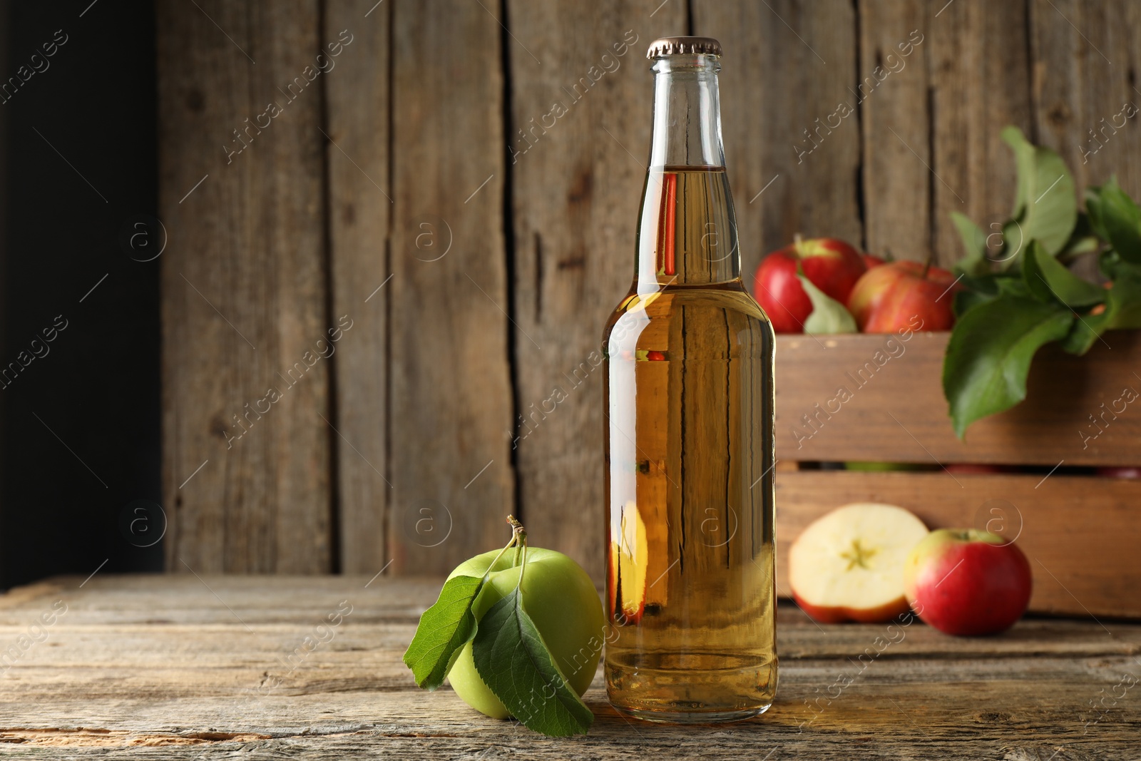 Delicious cider in glass bottle and apples on wooden table Photo of Delicious cider in glass bottle and apples on wooden table