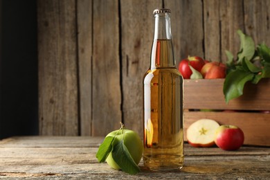 Photo of Delicious cider in glass bottle and apples on wooden table
