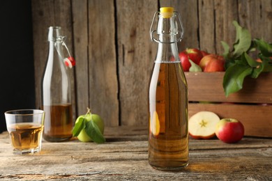 Photo of Delicious cider in glass bottles and apples on wooden table