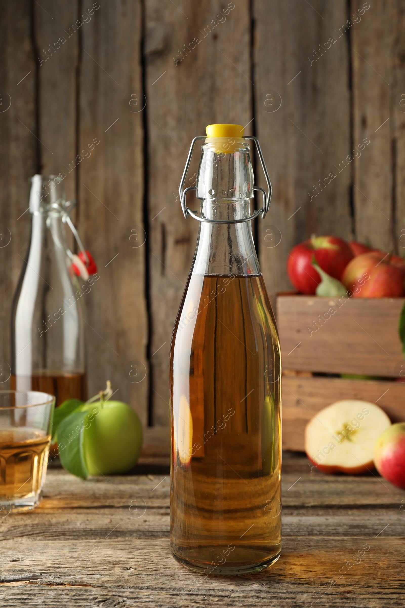 Delicious cider in glass bottle and apples on wooden table, closeup Photo of Delicious cider in glass bottle and apples on wooden table, closeup